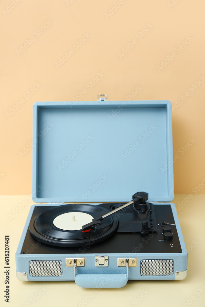 Record player with vinyl disk on table near beige wall