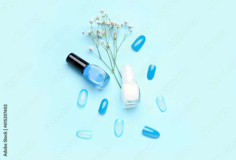 Press-on nails with polishes and flowers on blue background