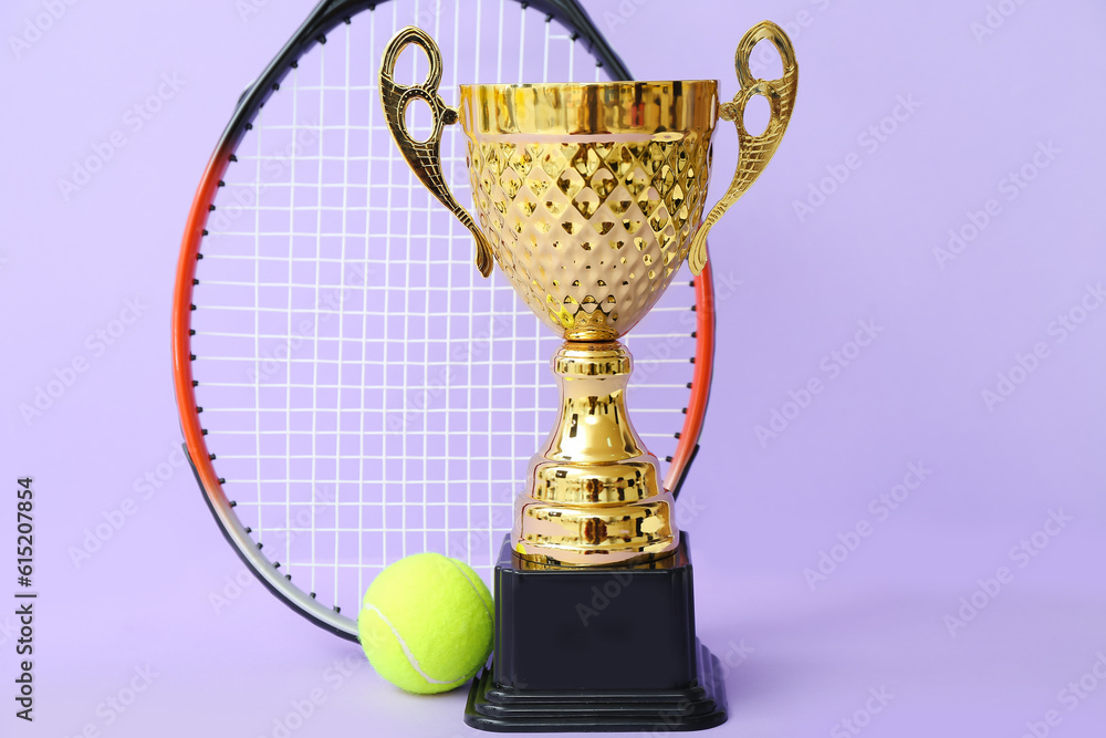 Gold cup with tennis racket and ball on lilac background