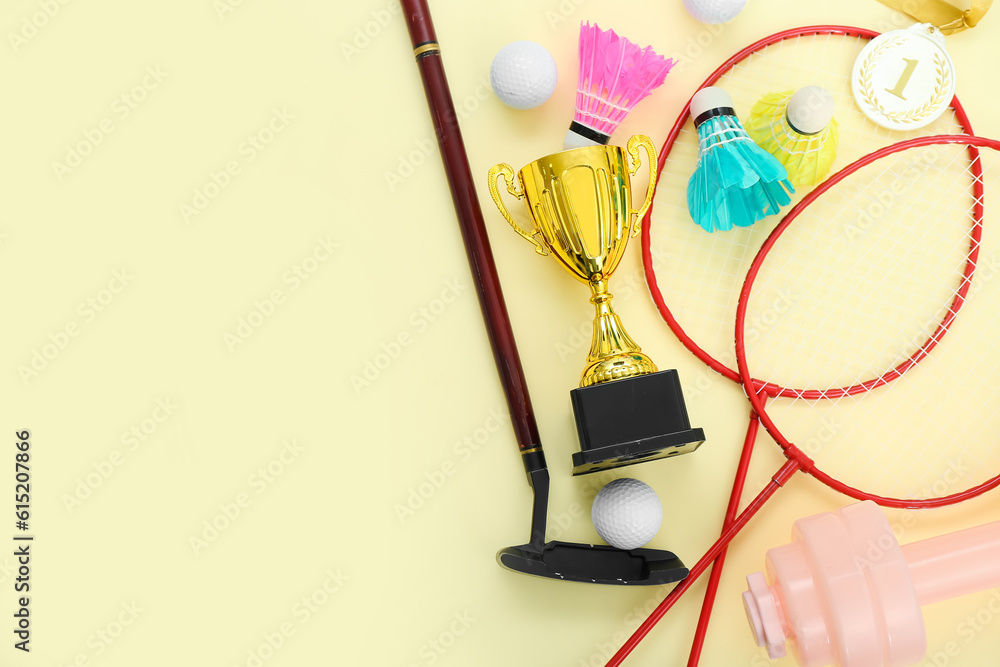 Gold cup with sports equipment on yellow background