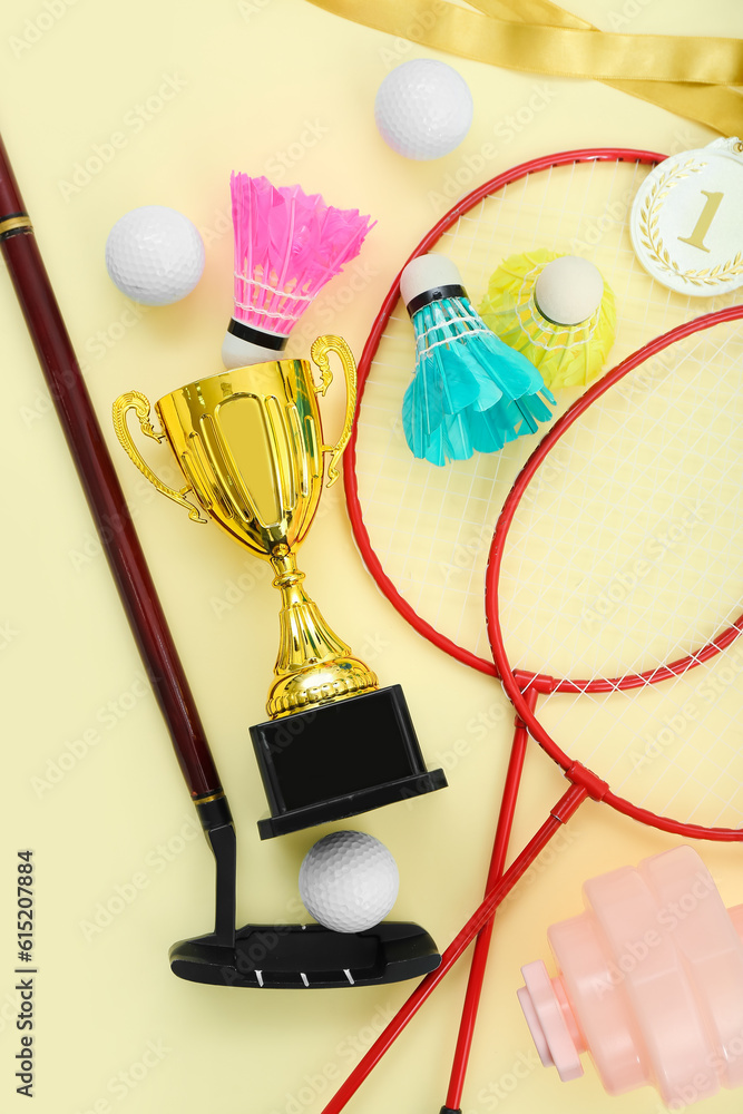 Gold cup with sports equipment on yellow background