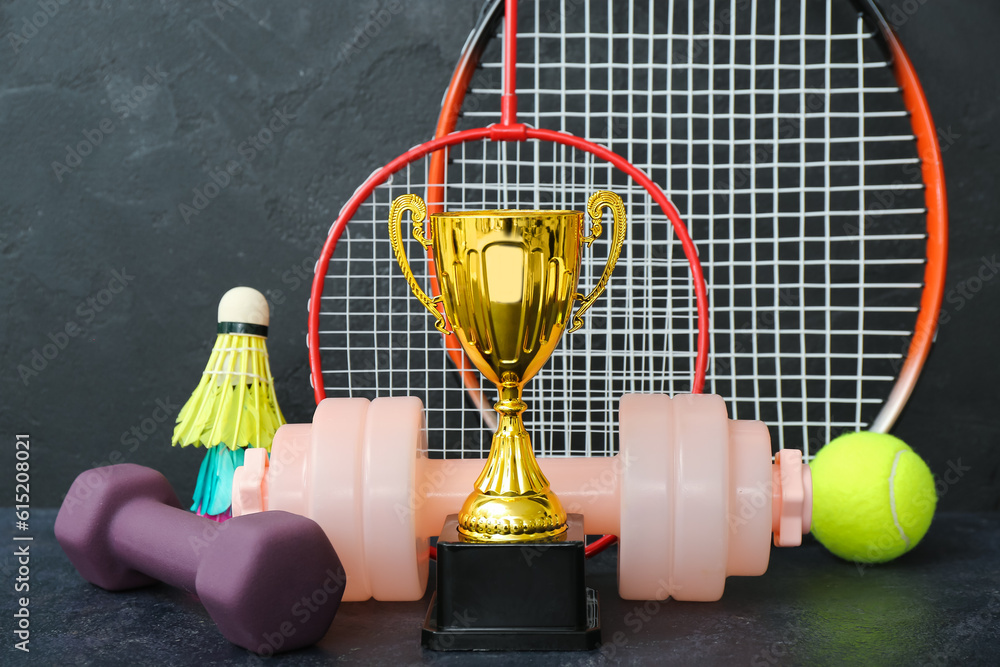 Gold cup with sports equipment on dark background