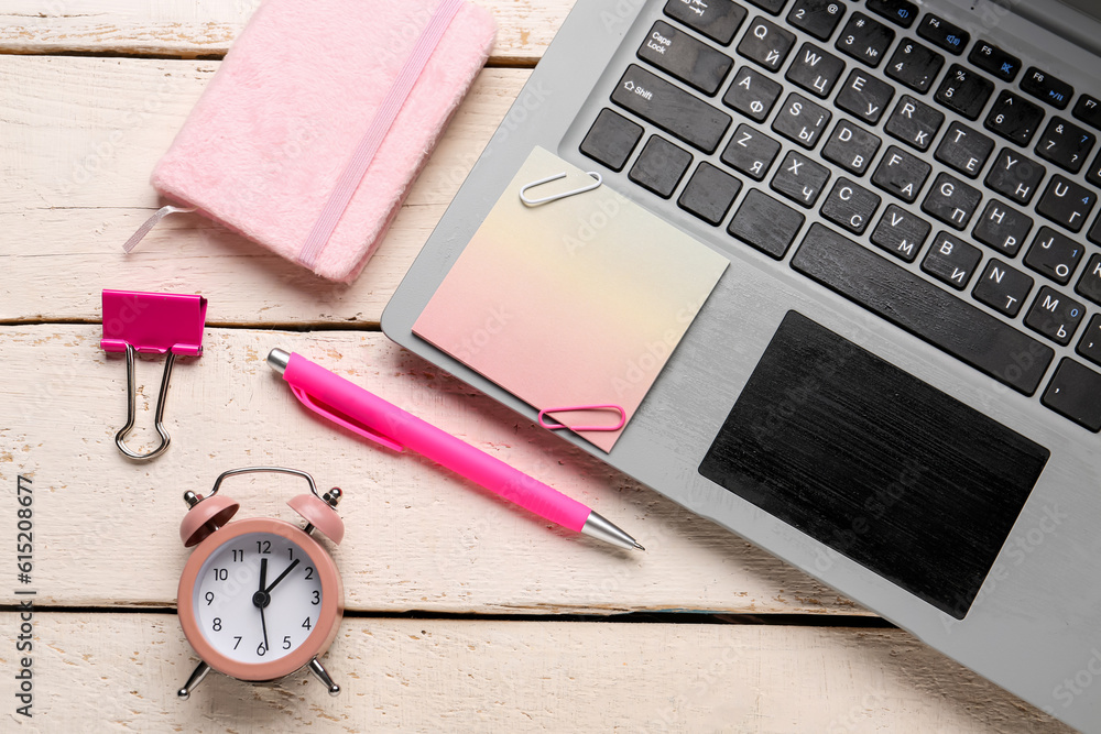 Composition with sticky note, laptop and clock on light wooden background