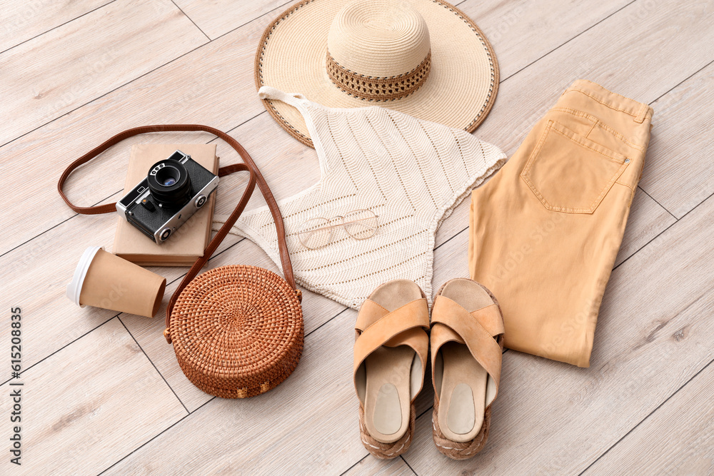 Summer clothes with accessories, cup of coffee and photo camera on light wooden floor