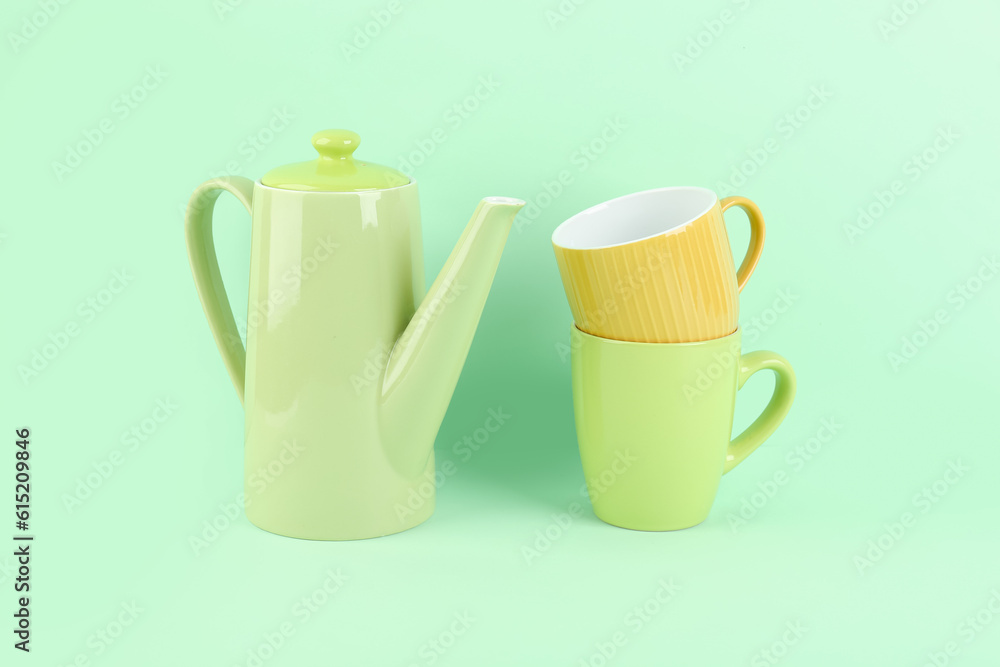 Teapot and mugs on green background