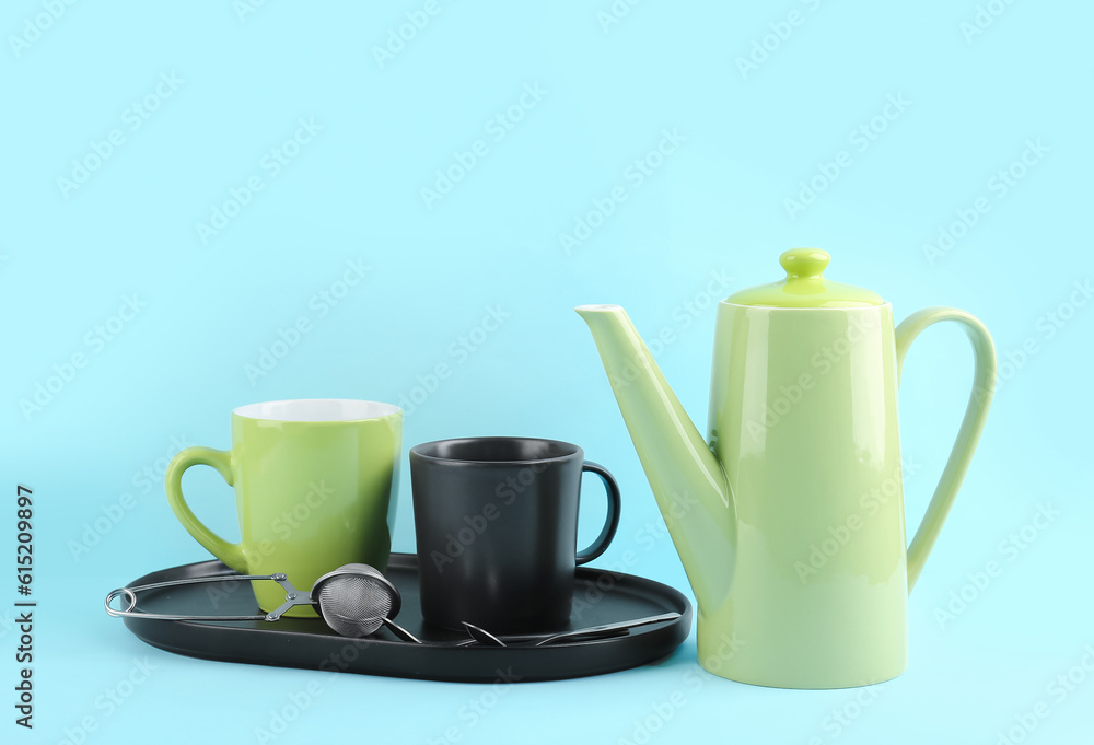 Teapot and tray with mugs on blue background