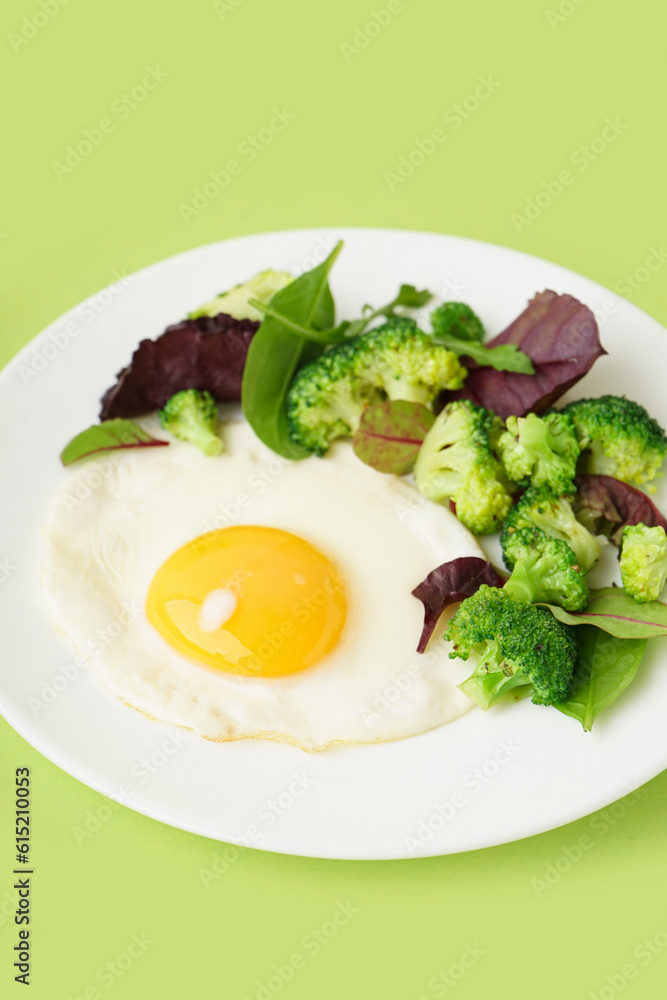 Plate with tasty fried egg, broccoli and spinach on green background