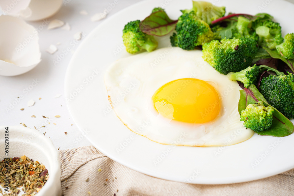 Plate with tasty fried egg, broccoli and spinach on light background