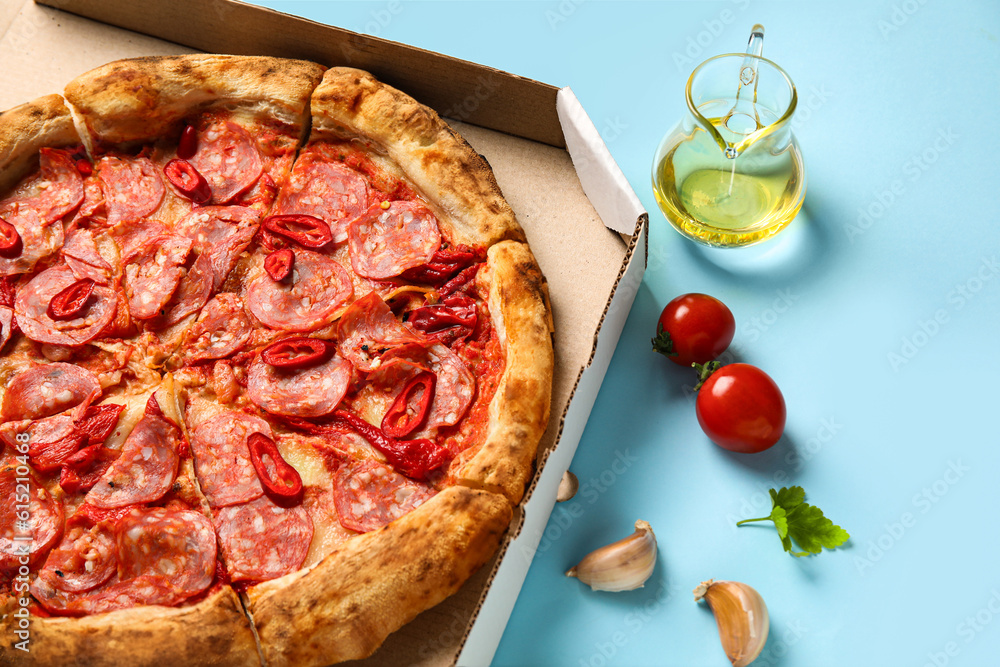 Cardboard box with delicious pepperoni pizza and ingredients on blue background