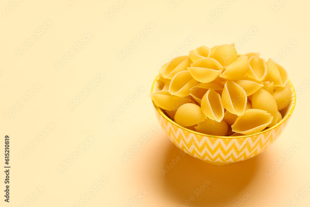 Bowl with raw conchiglie pasta on yellow background