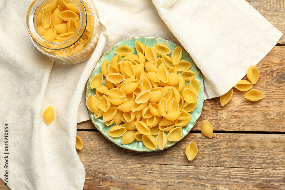 Plate and jar with raw conchiglie pasta on wooden background