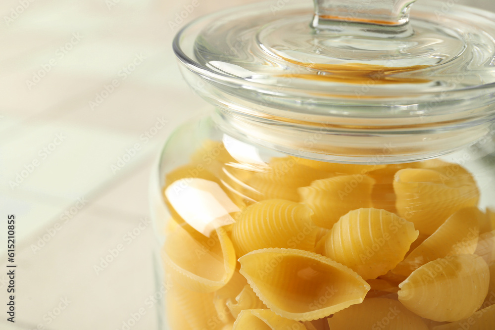 Jar with raw conchiglie pasta on table, closeup