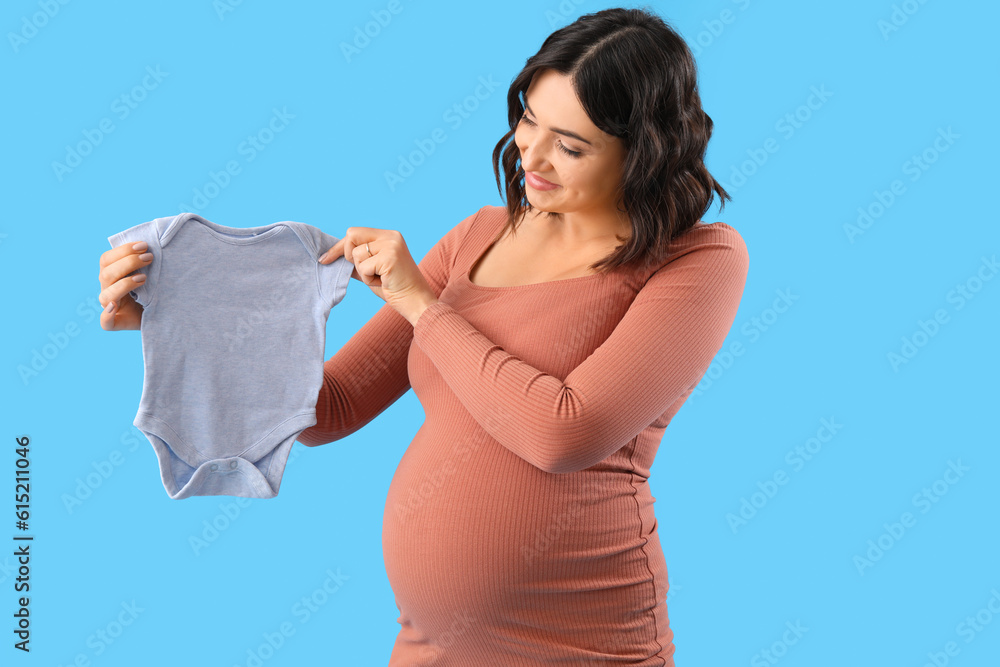 Young pregnant woman with baby bodysuit on blue background