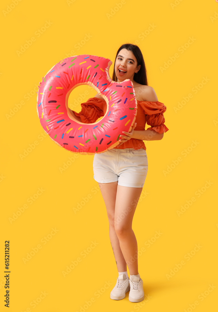 Young woman with inflatable ring in shape of doughnut on orange background