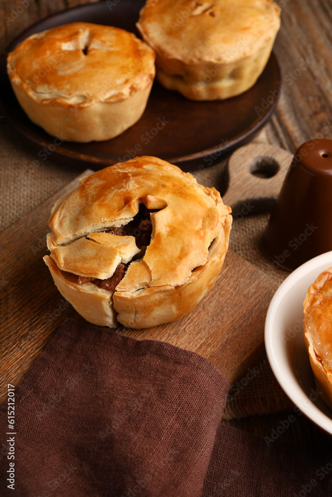 Wooden board with tasty meat pot pies on table