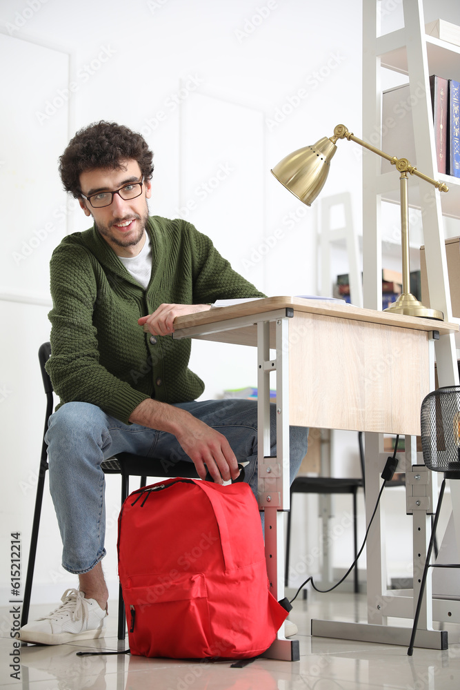 Male student with backpack sitting at table in library