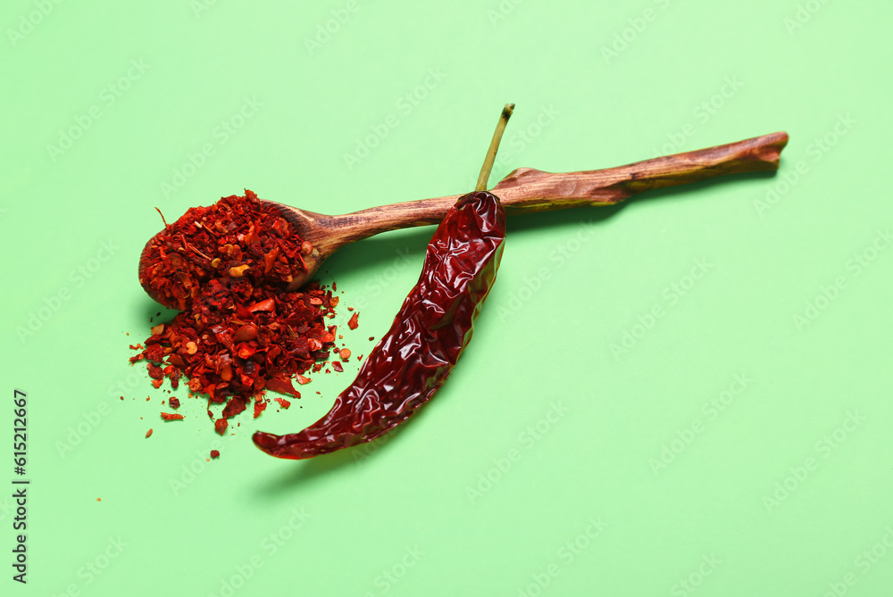 Wooden spoon with chili flakes on pale green background