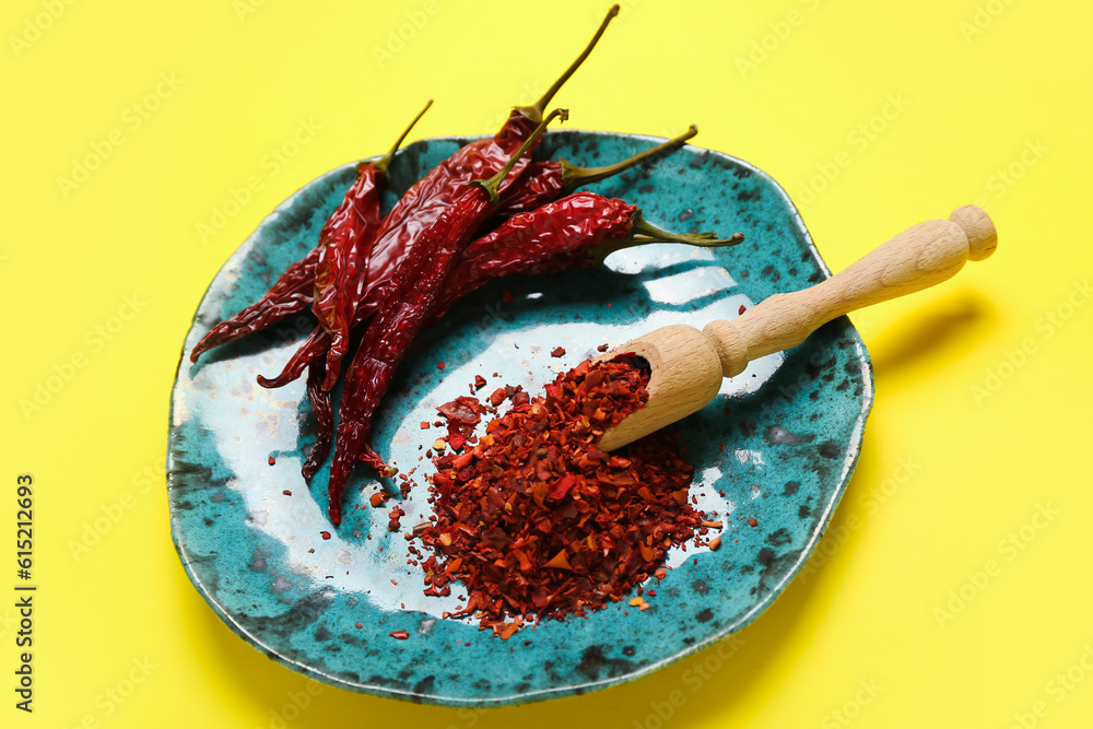 Plate with dry chili and ground  peppers on yellow background