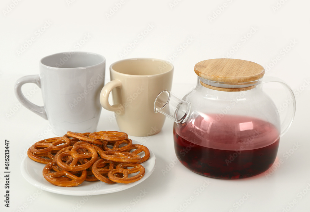 Plate of delicious pretzels and teapot with cups on white table