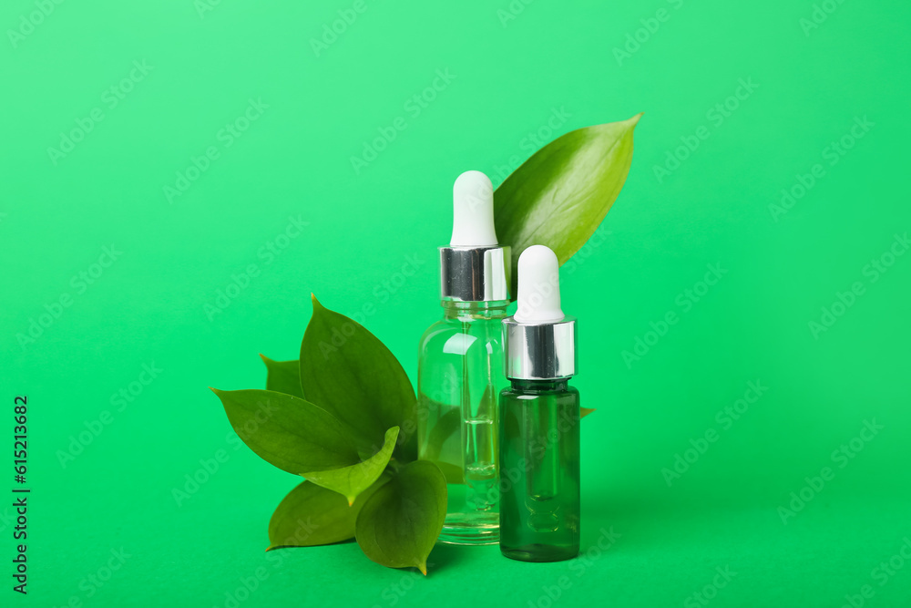 Bottles of cosmetic oil with plant leaves on green background