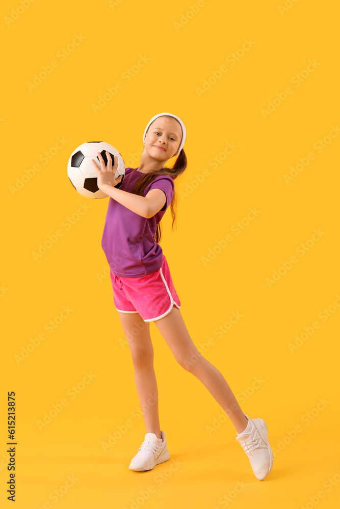 Sporty little girl with soccer ball on yellow background