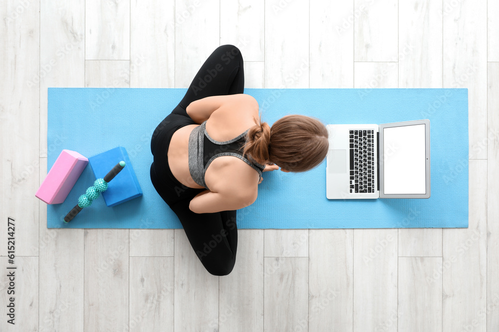 Sporty young woman with laptop doing yoga in gym, top view