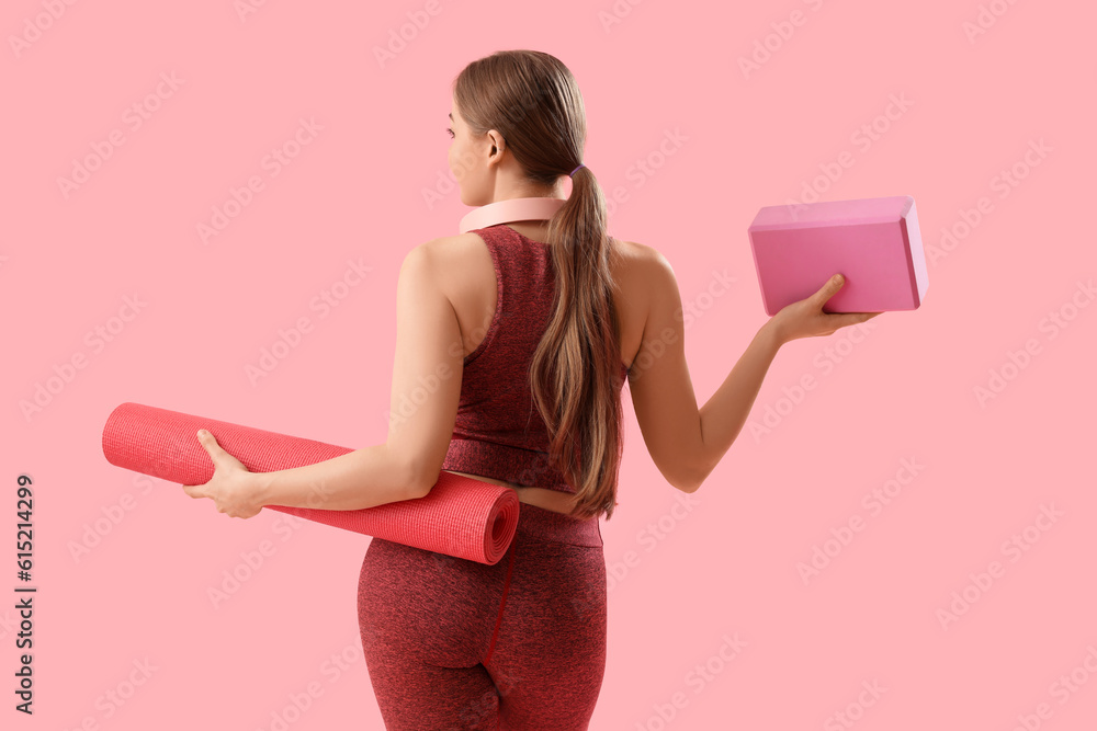 Sporty young woman with mat and block for yoga on pink background