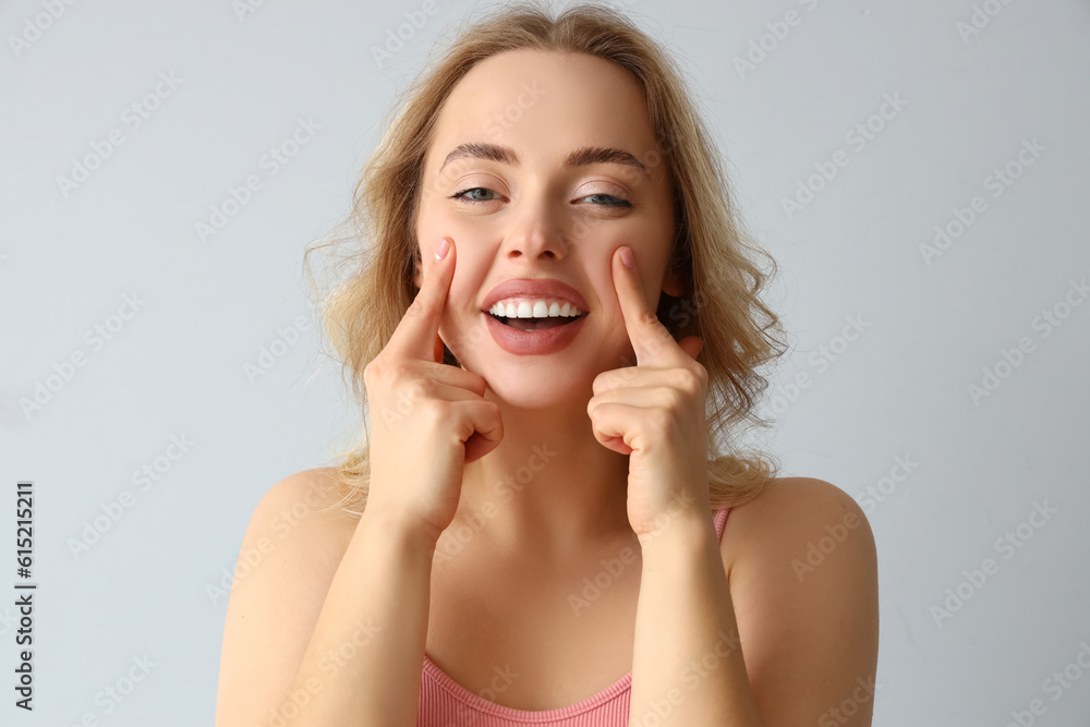 Young woman doing face building exercise on light background, closeup