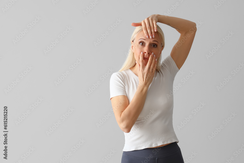 Mature woman doing face building exercise on light background