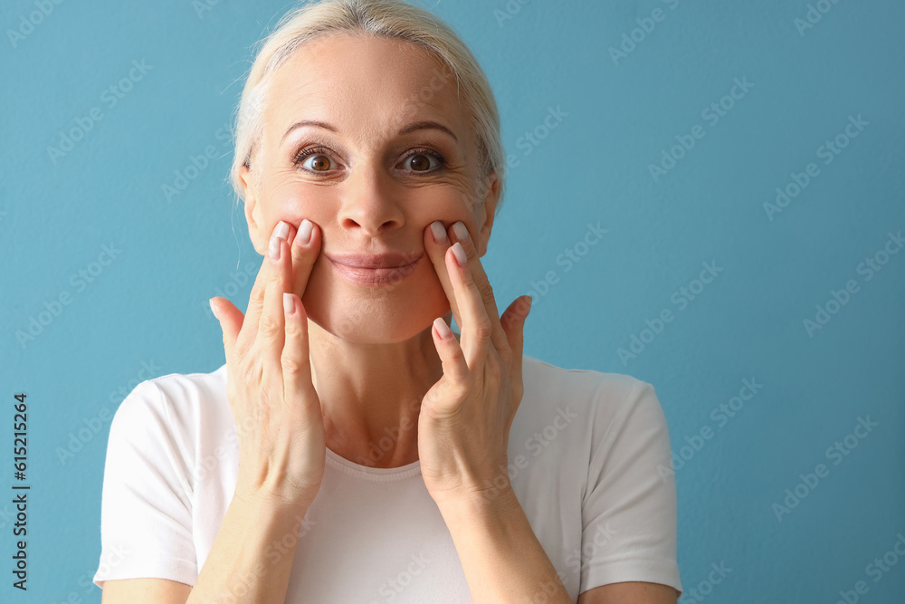 Mature woman doing face building exercise on blue background, closeup