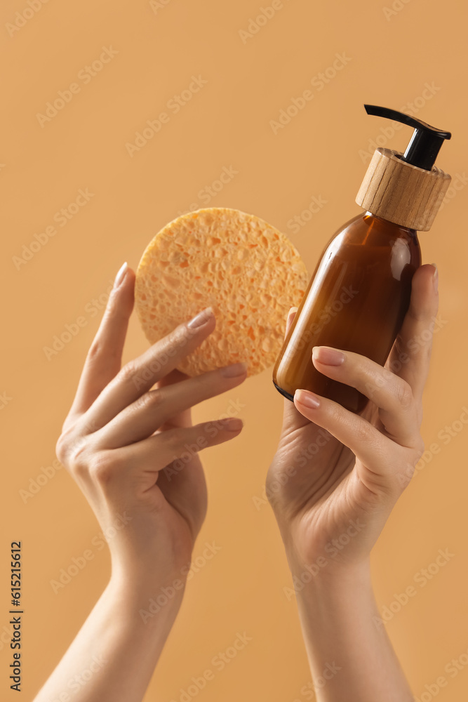 Hands holding cosmetic product and sponge for makeup removal on beige background