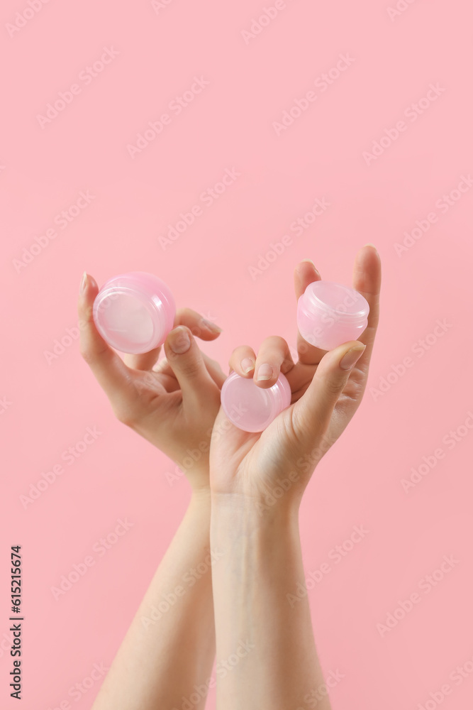 Hands holding jars of cosmetic cream on pink background