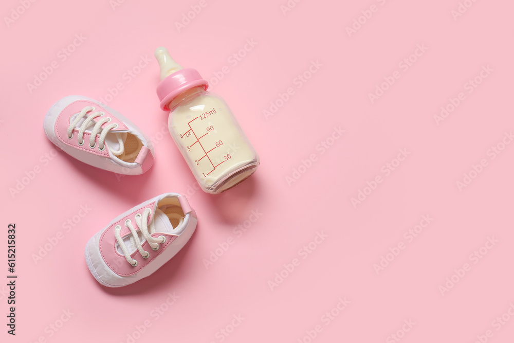 Bottle of milk for baby with booties on pale pink background