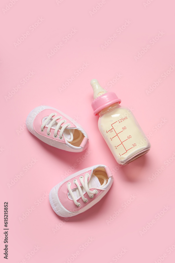 Bottle of milk for baby with booties on pale pink background