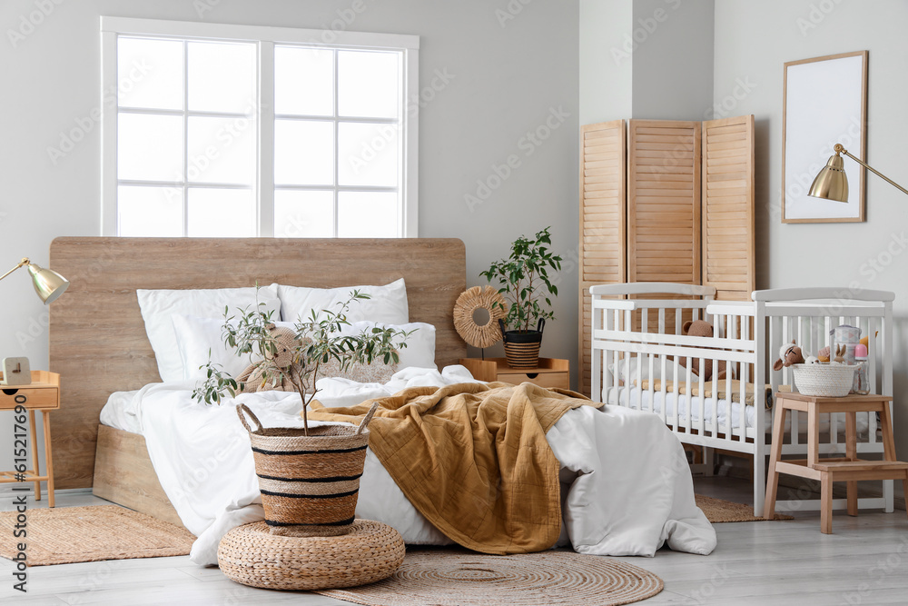 Interior of light bedroom with bed and baby crib