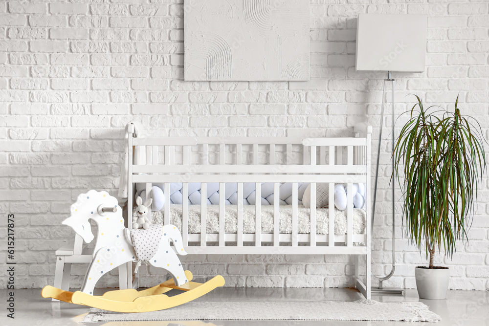 Interior of light bedroom with baby crib, toys and lamp