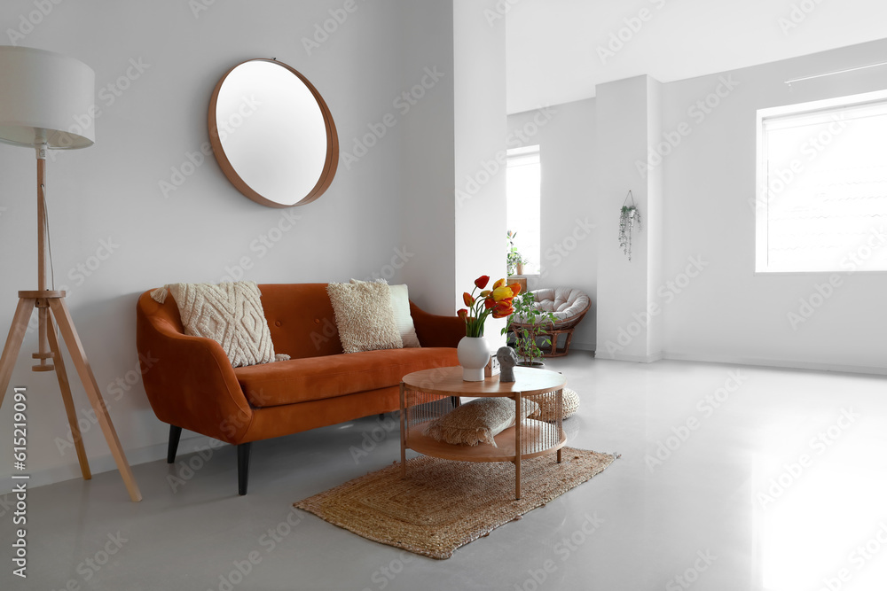 Interior of stylish living room with cozy sofa, mirror and tulip flowers on coffee table