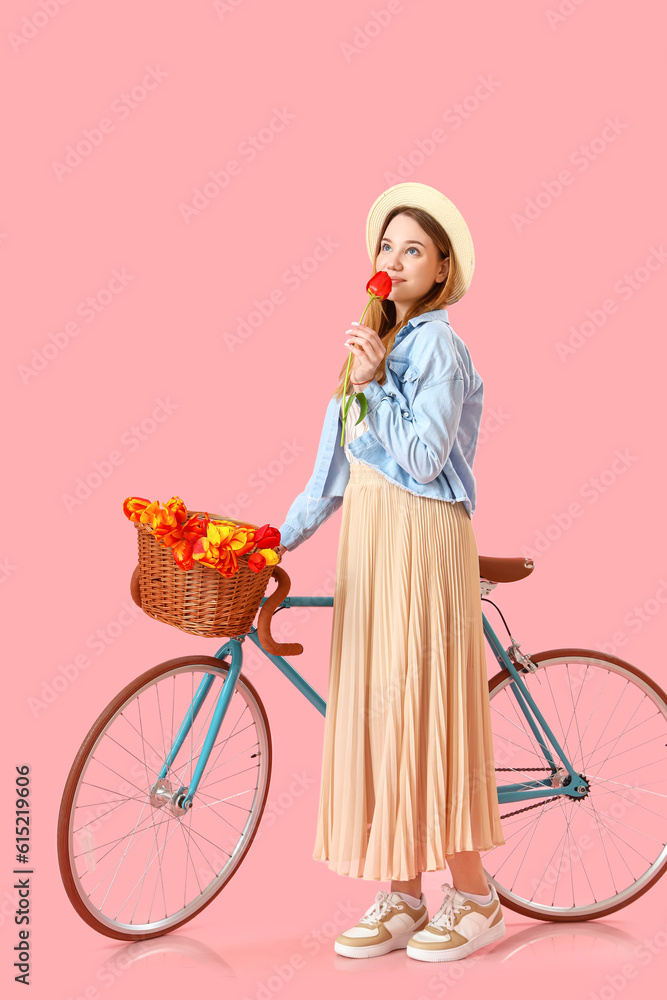 Young woman with bicycle and tulip on pink background