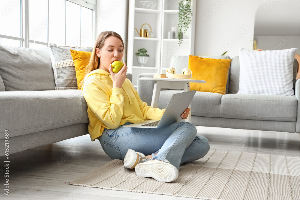 Female student with laptop eating apple at home