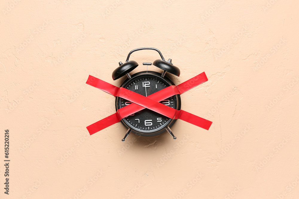 Alarm clock with cross made of adhesive tape on beige background