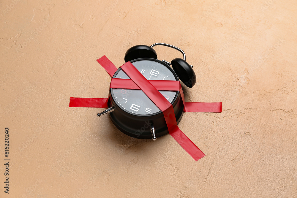 Alarm clock with cross made of adhesive tape on beige background