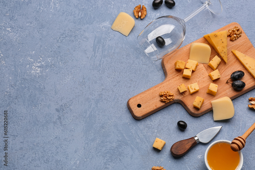 Wooden board with pieces of tasty cheese, wine glass and honey on grey background