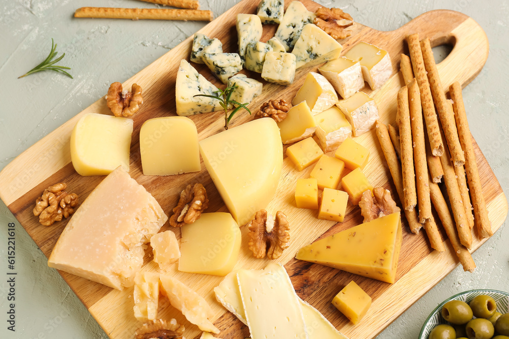 Wooden board with pieces of tasty cheese on light background