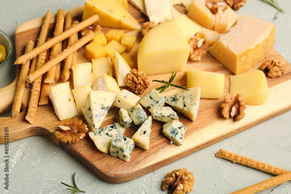 Wooden board with pieces of tasty cheese on light background