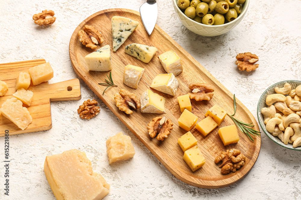 Wooden board with pieces of tasty cheese on light background