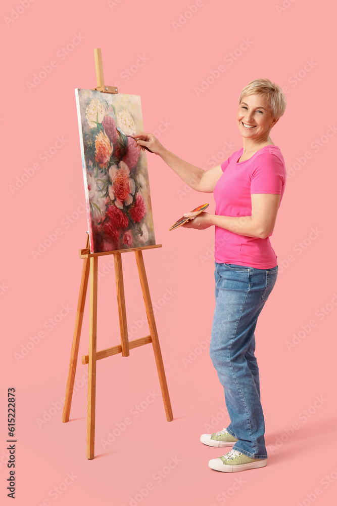 Mature female artist painting picture on pink background