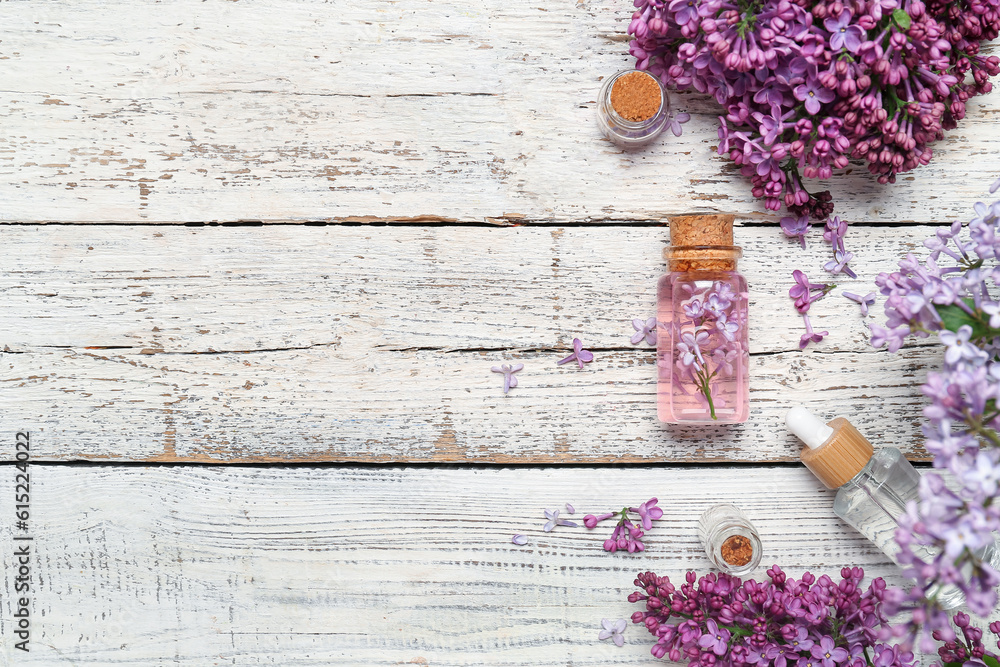 Composition with bottles of lilac essential oil and flowers on light wooden background