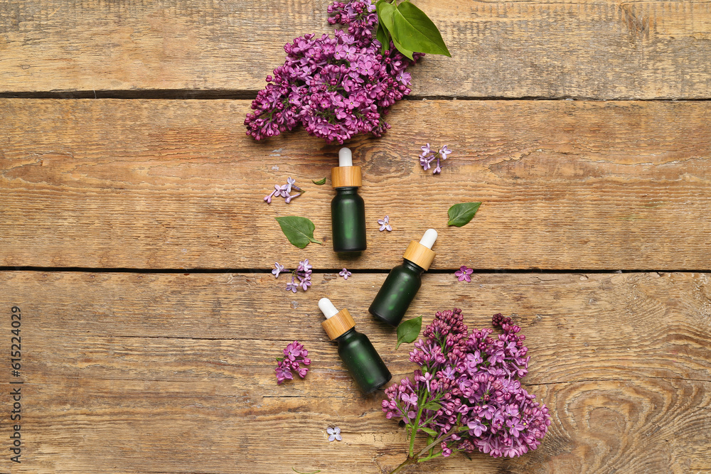 Bottles of lilac essential oil and flowers on wooden background