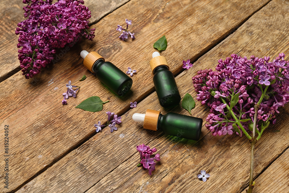 Bottles of lilac essential oil and flowers on wooden background, closeup