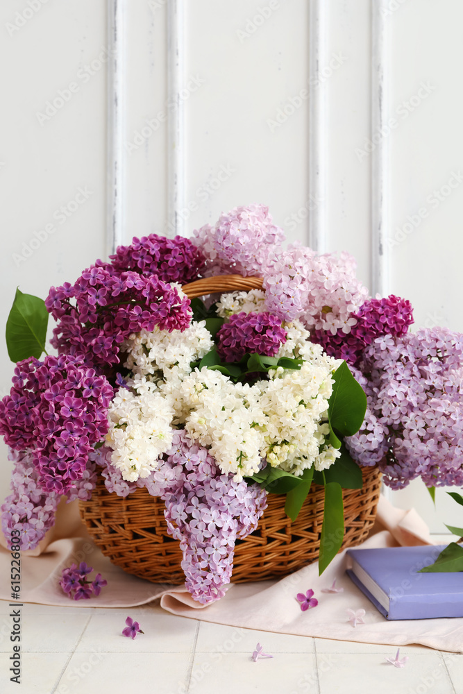 Wicker basket with beautiful fragrant lilac flowers near white wooden wall